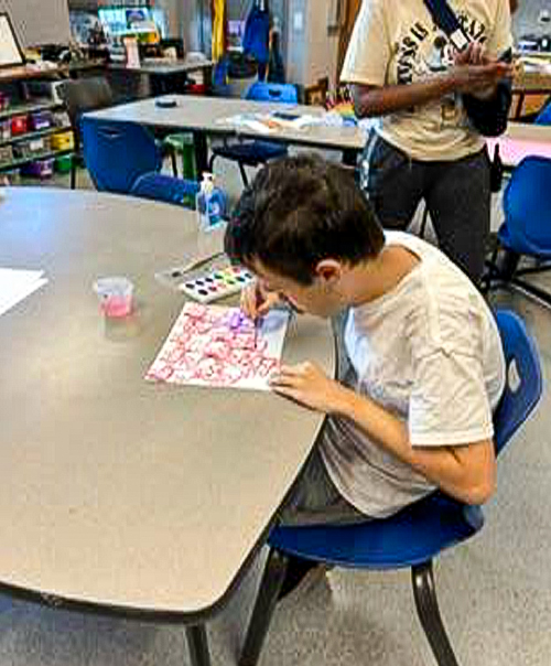 Youth male at a table drawing a picture with a pink marker