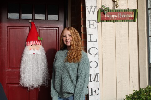 Molly poses in front of a front door to a house, decorated for Christmas.