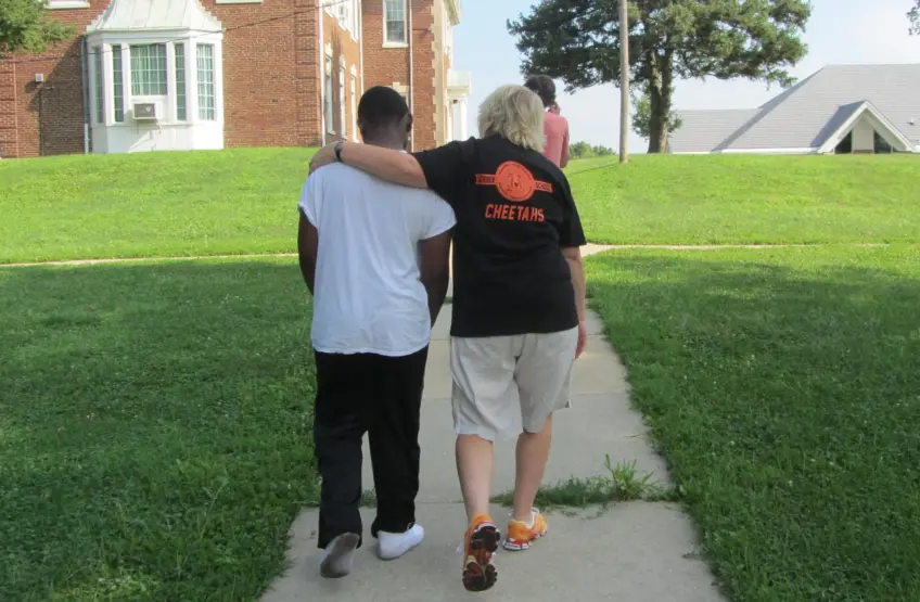 photo from behind of a staff member walking with a male youth with her arm around him