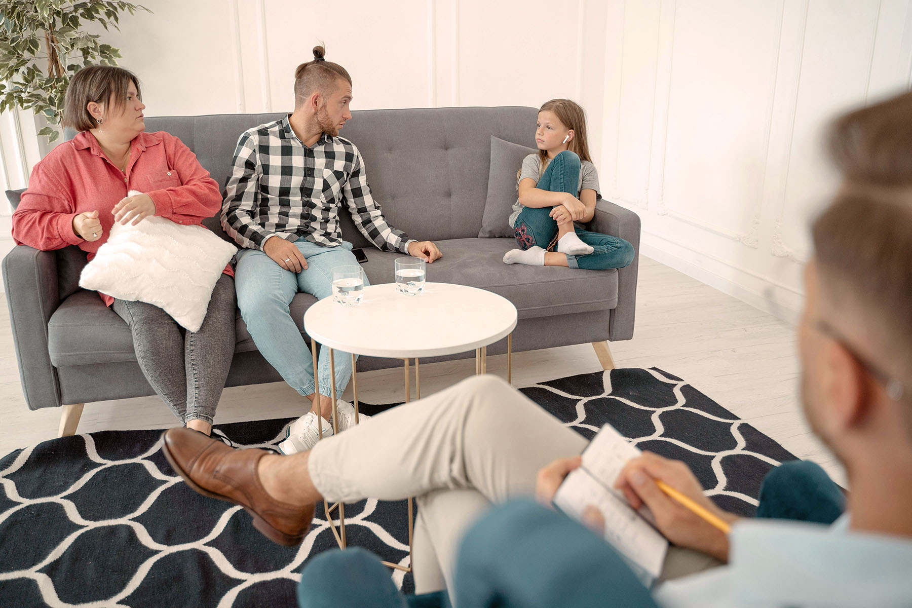 Mother, Father sitting next to each other with their daughter also on the couch but further away and all three are looking at each other as therapist sits across