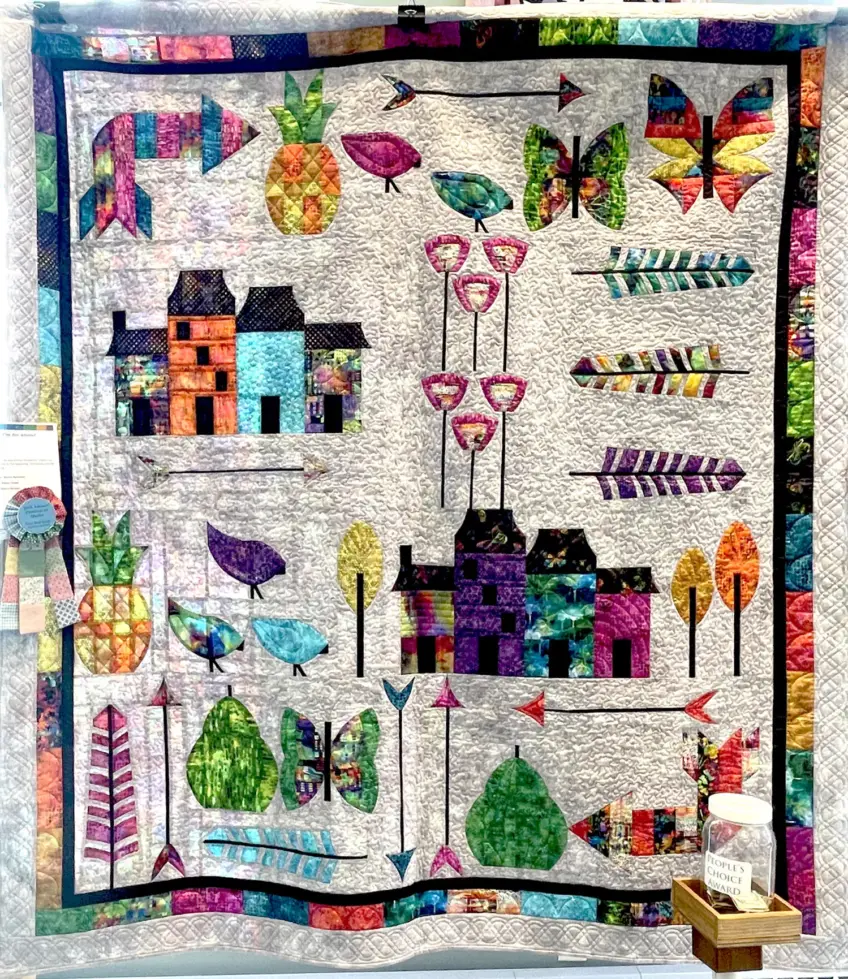 Rich looking quilt with silvery background and border of vibrant, metallic like pink, blue, yellow, green. Interior has gorgeous images of butterflies, buildings, birds  and fruits