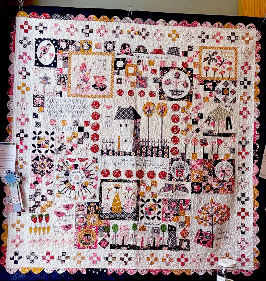 Wall hanging with black backing that borders a cream interior with blocks including delightful images like butterflies and floweres in colors of yellow, pink, red and black