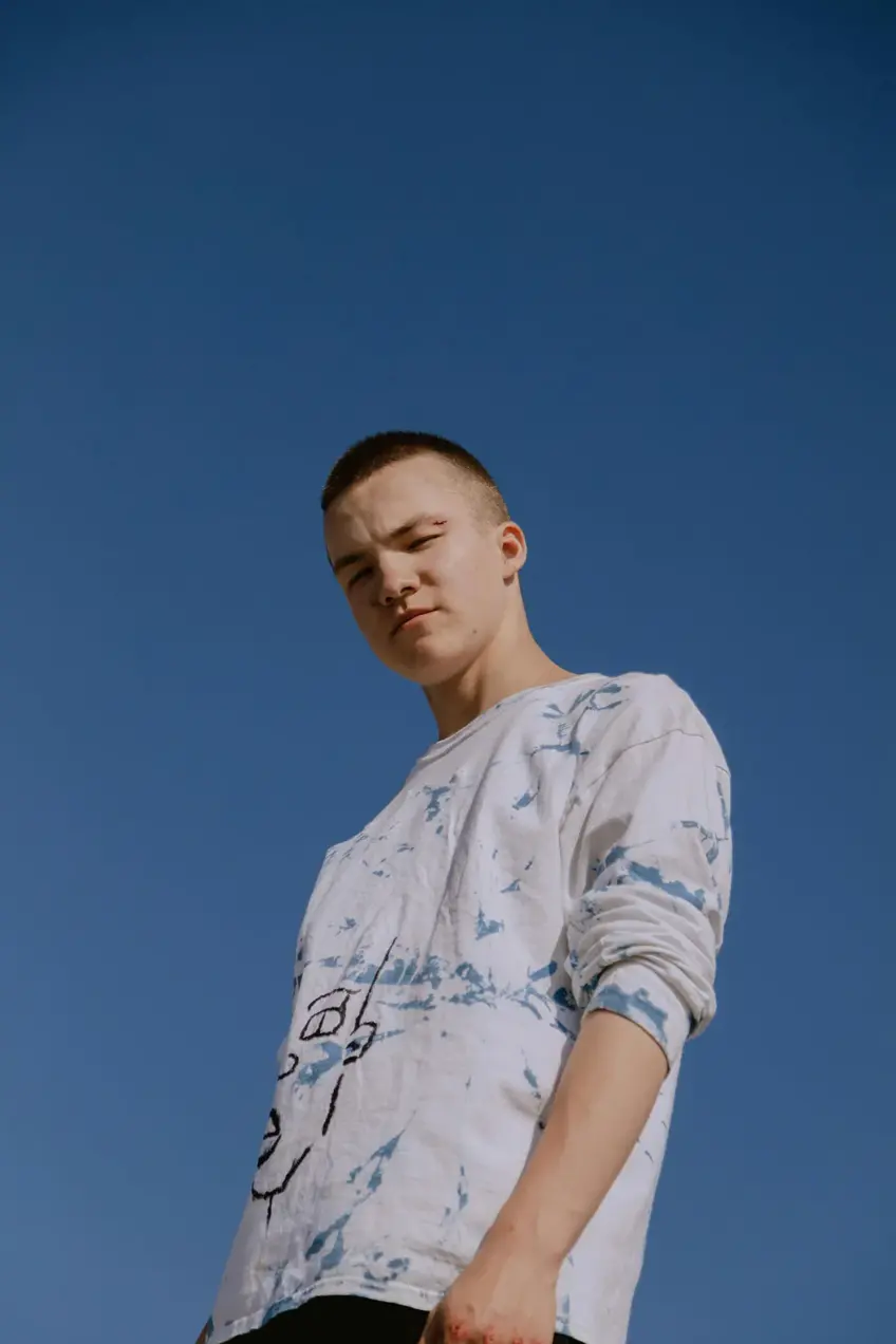 Teenage boy in white graphic tshirt standing in front of a blue sky.