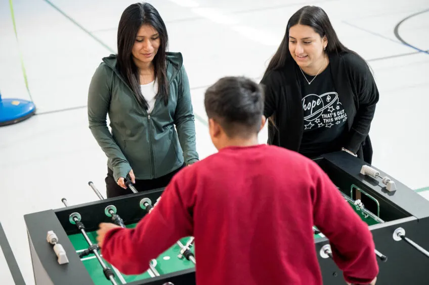 Two female youth care professionals playing foosball with a Caminos youth. 