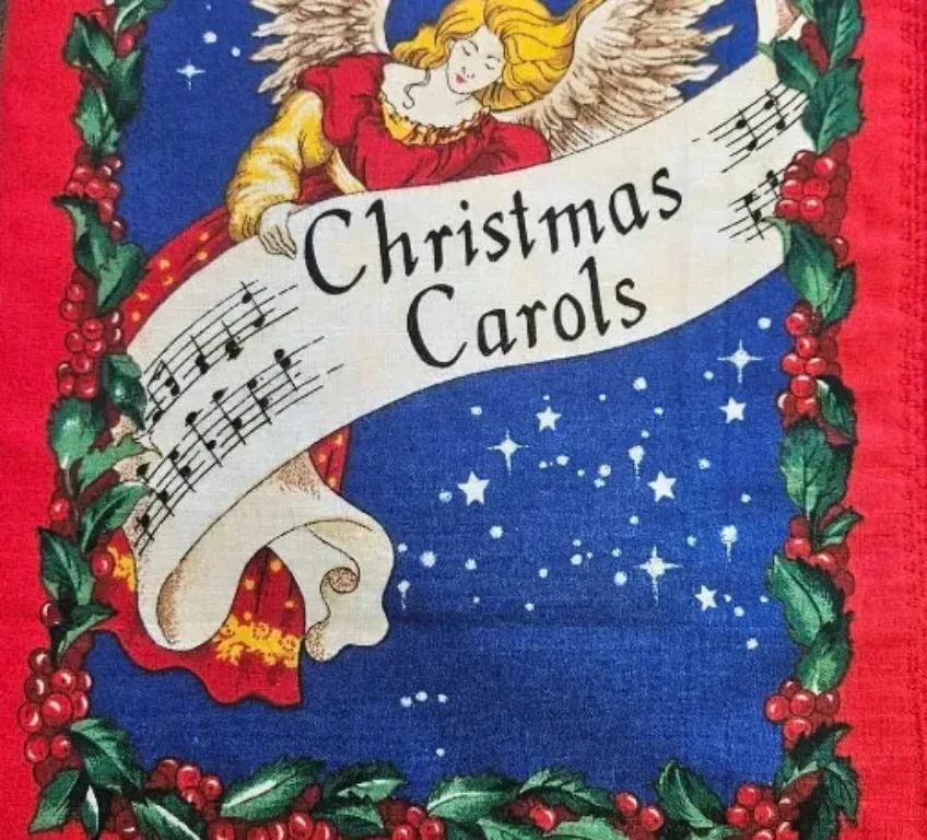 Christmas carols fabric book with red border, Christmas holly, an angel in a red and yellow dress and a blue sky background with stars