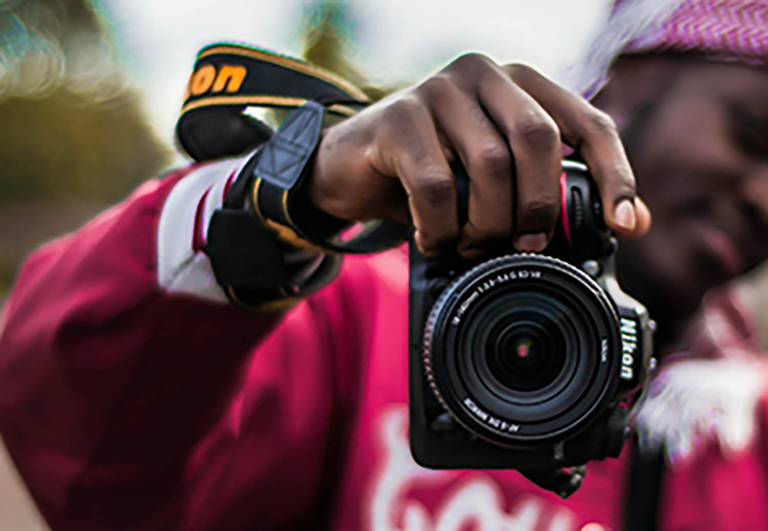 male teenager wearing a red jacket and holding up a Nikon camera in front of his body