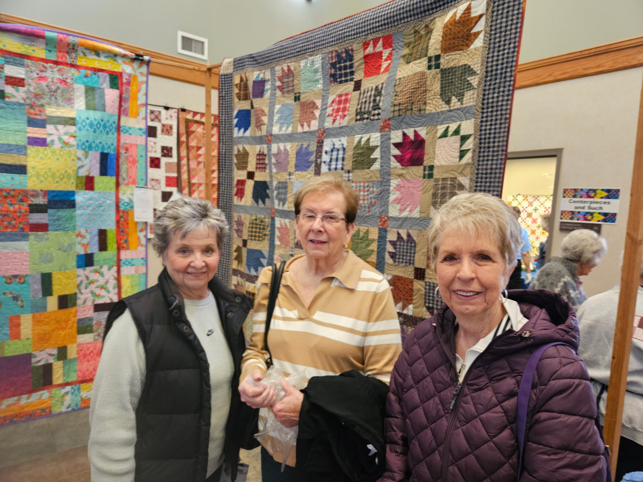 three women standing in front of hanging quilts