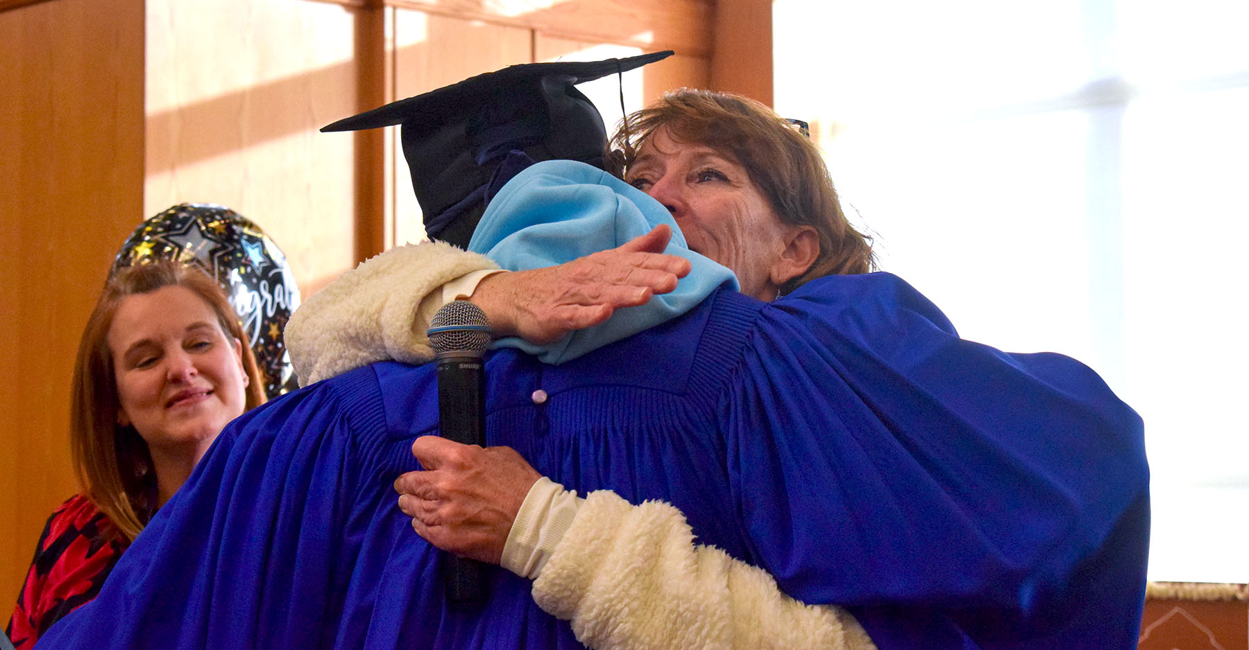 Assistant principal hugging a graduate while principal gazes with pride at them.