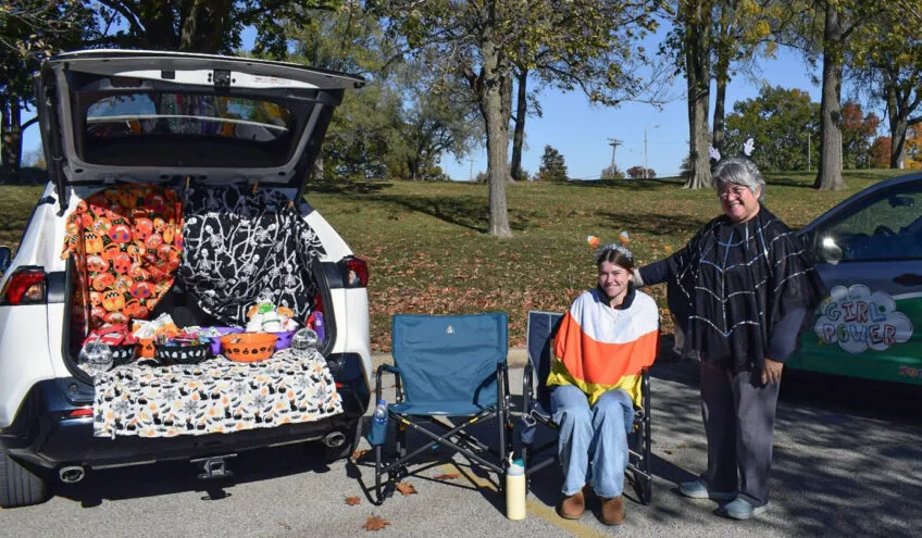an older woman and younger girl standing next to their trunk which is open and decorated for Halloween and has bowls full of candy for Trunk or Treat
