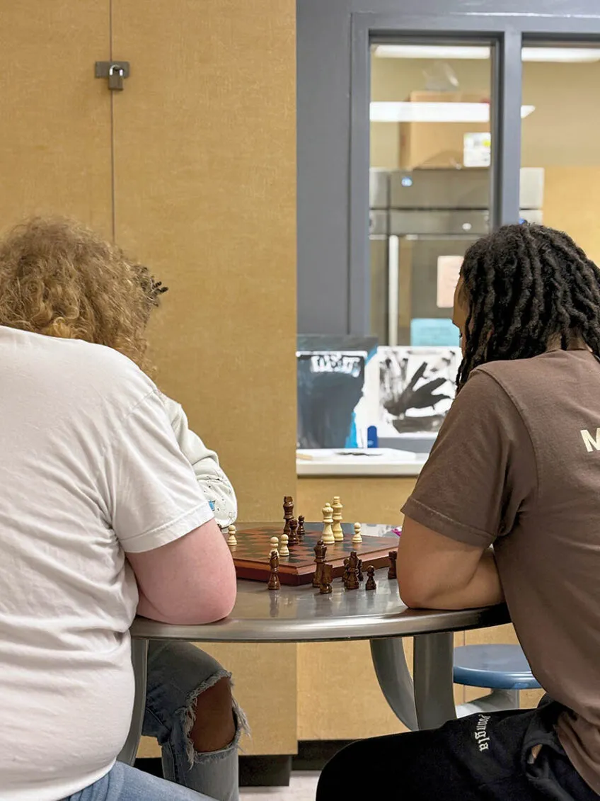 a teenager and a young adult playing chess on a silver round dining table from the backside